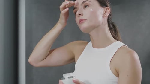 Woman Applying Moisturizer in Bathroom Mirror