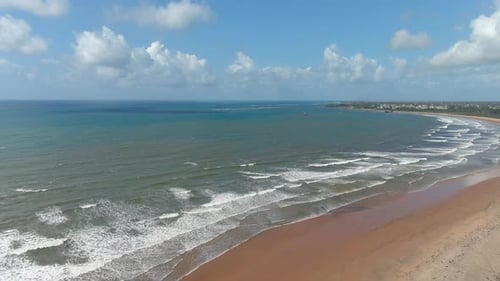 backward aerial view of a large sandy bay where white foamy waves arrive on the shore. wide shot