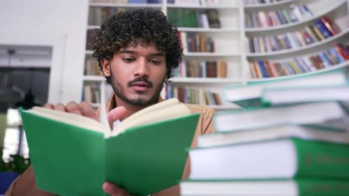 Close up of student learning reading books in campus library space. Male is studying