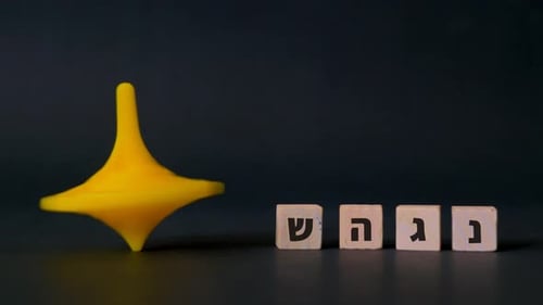 Una peonza de plástico de Hanukkah gira junto a las cuatro letras hebreas nun, gimel, heh y shin que se muestran
