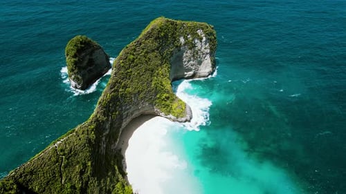 Pristine white sandy shore on tropical Island with huge green rock by the ocean. Kelingking beach in