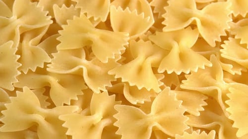 Authentic italian dry pasta farfalle rotating closeup background top view sunny. Raw dried organic