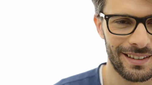 Un jeune homme souriant dans des lunettes regarde avec confiance la caméra sur fond blanc