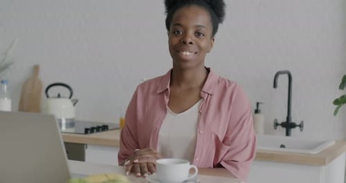 Smiling Woman in Kitchen with Laptop and Coffee
