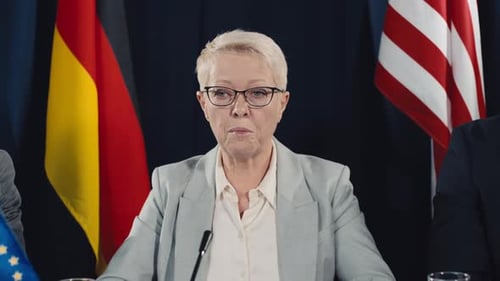 Woman Speaking at a Press Conference, Flags Behind