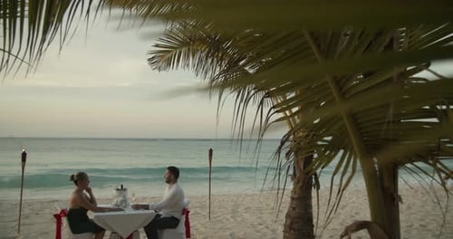 Romantic sunset dinner on tropical beach pan down from palm trees in slow motion