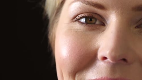 Closeup of a female eye blinking on dark studio background