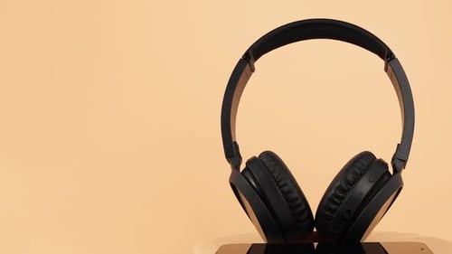 Los auriculares inalámbricos negros giran sobre un fondo naranja.