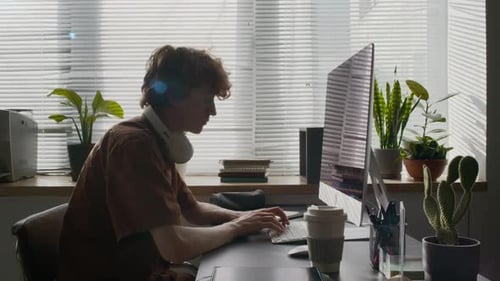 Young Developer with Headphones around Neck Working on Computer in Office