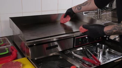 Closeup of the Chef Putting Burger Patties on a Stove in the Restaurant Kitchen