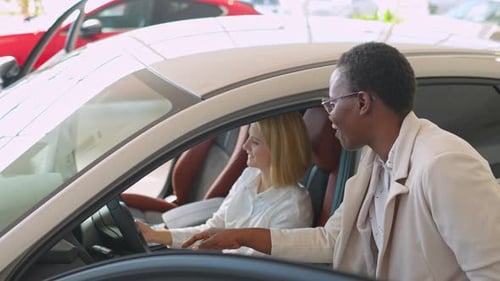 African american car salesman shows a caucasian woman a new car in a dealership