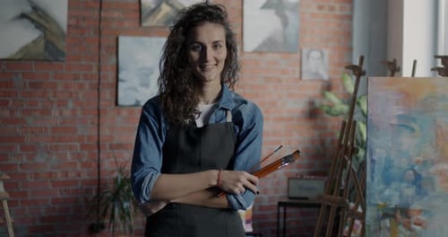 Portrait of Female Artist Creative Lady in Apron Standing in Workshop Near Easel Holding Paintbrush