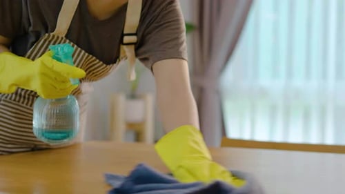 Close-up of hand woman in gloves and apron polishing or wiping wooden table