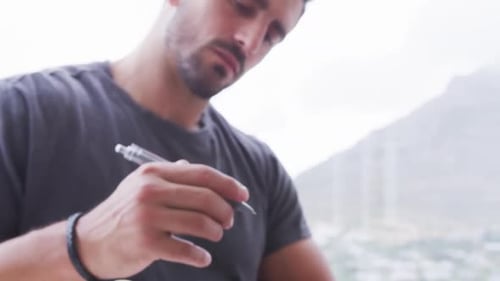Man locating page in notebook, tapping pen and journaling beside window mountain view and wristband