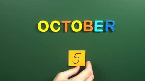 Hand sticking a sticker 5 October calendar day on school board. 5 date of October. Fifth day