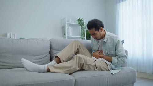 Asiatische attraktive kranke Männer leiden im Wohnzimmer unter Magenschmerzen.