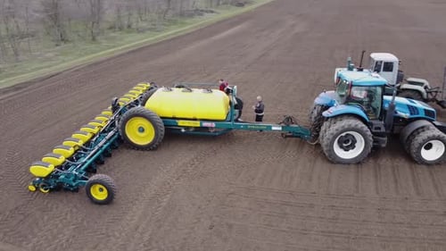Blue tractor with yellow seeder working on the field in Ukraine OA