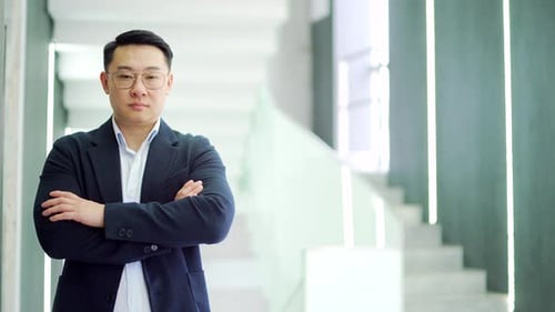 Portrait of a serious asian businessman in a formal suit standing in a modern office building.