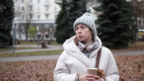Portrait of Mature Woman in Wool Hat Standing on the Urban Street with Mobile Phone in Hand