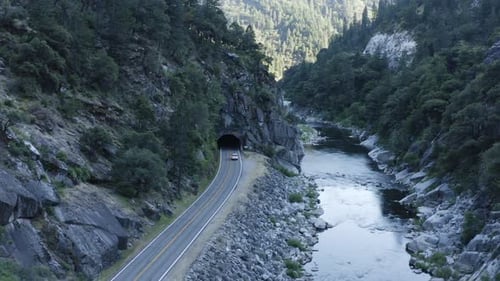 Aerial following car on canyon road entering dark tunnel through rocky mountain