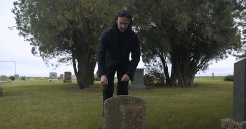 Sad, emotional, distraught man kneeling at grave to mourn in cemetery.