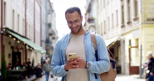 Cheerful Young Handsome Man in Glasses Standing at Street on Nice Day and Texting Message on