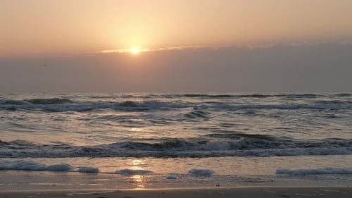 Gentle waves roll on a serene beach at sunrise with golden light reflecting on the water