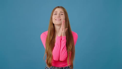 Young Woman Clasping Hands, Hoping on Blue Background