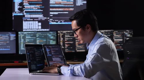 Programador examinando o banco de dados no tablet e escrevendo código em um laptop usando vários monitores