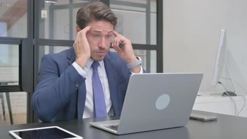Stressed Businessman Working on Laptop in Modern Office