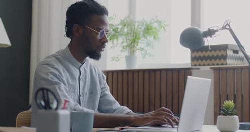 Vue latérale d'un employé travaillant avec un ordinateur portable concentré sur le travail de bureau assis à son bureau contre une fenêtre