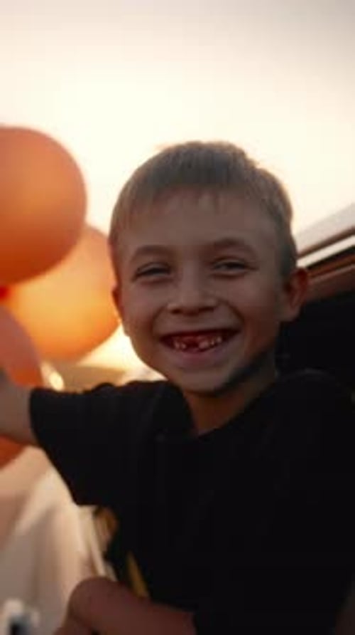 Joyful Little Boy with Balloons in Hand and Funny Smile Without One Teeth Smiling When Riding Car