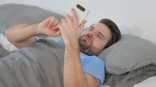 Man Lying on Bed Using Smartphone