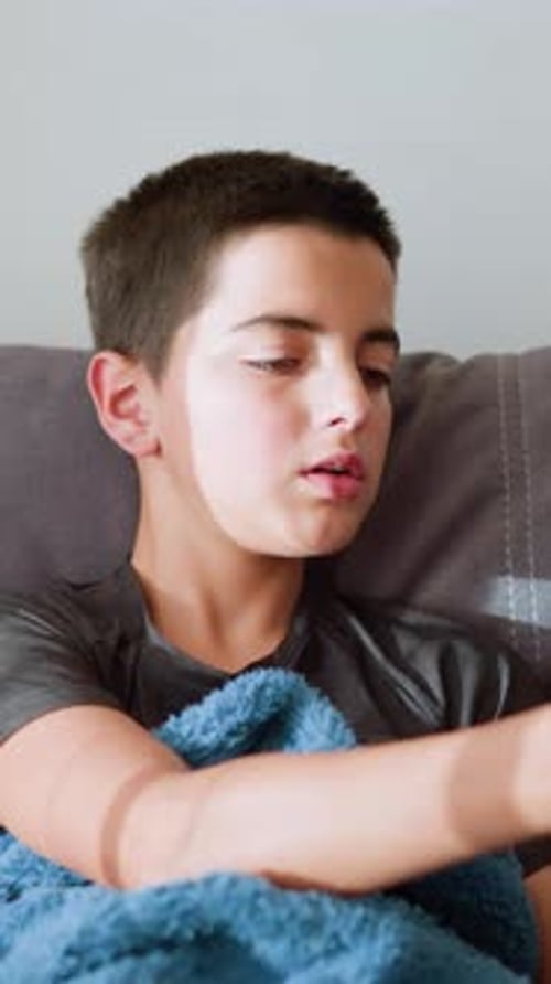 Boy Reaches for Thermometer to Check His Temperature While Lying on Couch