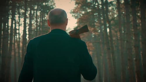 Adult Man Maniac Walking with Axe Mankiller Between Dark Trees in Forest Spooky Murderer Ready for