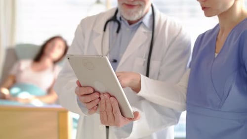 Unrecognizable doctor with tablet talks to nurse in hospital room