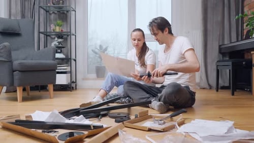 The wife helps her husband to assemble furniture by reading instructions to him.