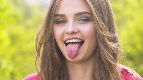 Beautiful Young Woman Smiles and Sticks out Tongue