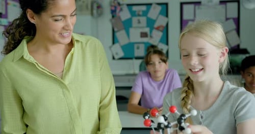 Female Science Teacher Explaining a Molecular model to School girl in Classroom