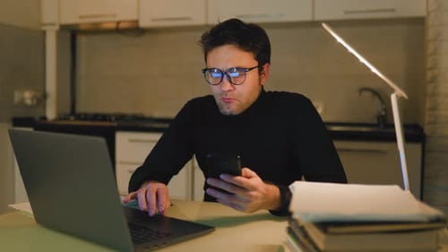 Working Late at Night in Kitchen with Laptop and Smartphone in Hand