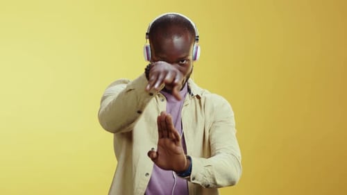 A Man Dances Joyfully in Headphones Against a Vibrant Yellow Background