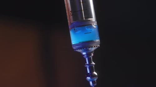 Extreme Nahaufnahme: Blaue Flüssigkeit wird in eine Spritze auf dunklem Hintergrund gezogen. Das Konzept der Dunklen Materie und