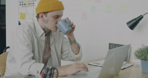 Creative Young Businessman Working with Laptop and Drinking Coffee in Office