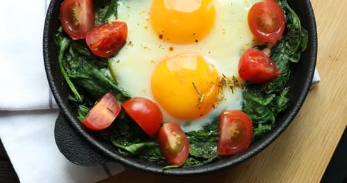 Œufs frits aux épinards et tomates dans une poêle sur la table, vue de dessus