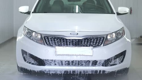 Worker in Garage Automobile Service is Washing a Car in the Suds By Noncontact High Pressure Water