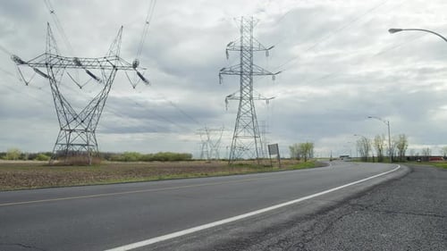 Transmission Tower With Overhead Power Lines And Asphalt Road In Foreground. - wide sshot