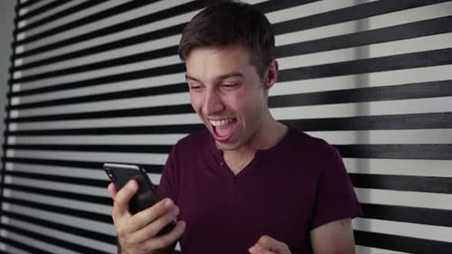 Man Cheers While Looking at His Mobile Phone