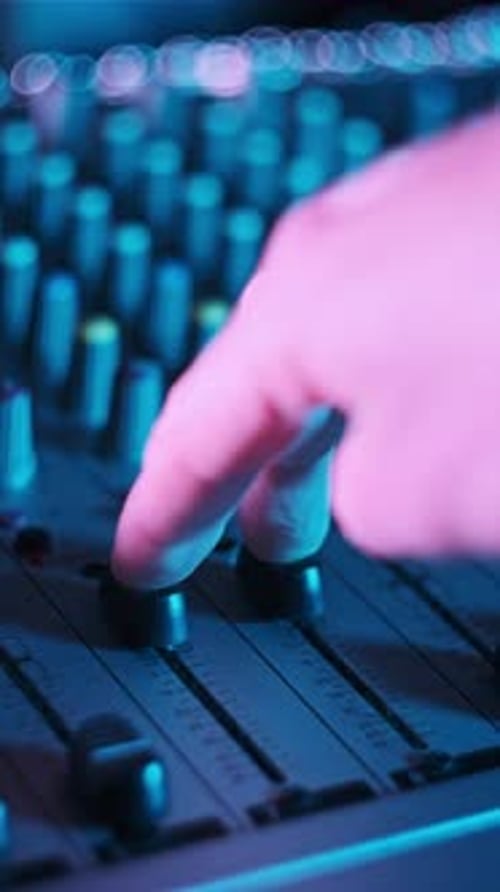 Vertical Hand Adjusts Volume Level Controls on Mixing Console Faders in Neon