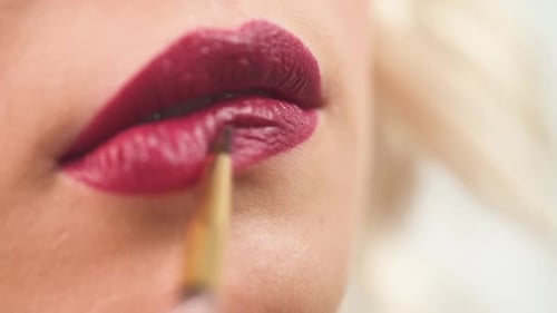 Visagistin beim Beauty-Shooting malt die Lippen eines Mädchenmodels in Nahaufnahme
