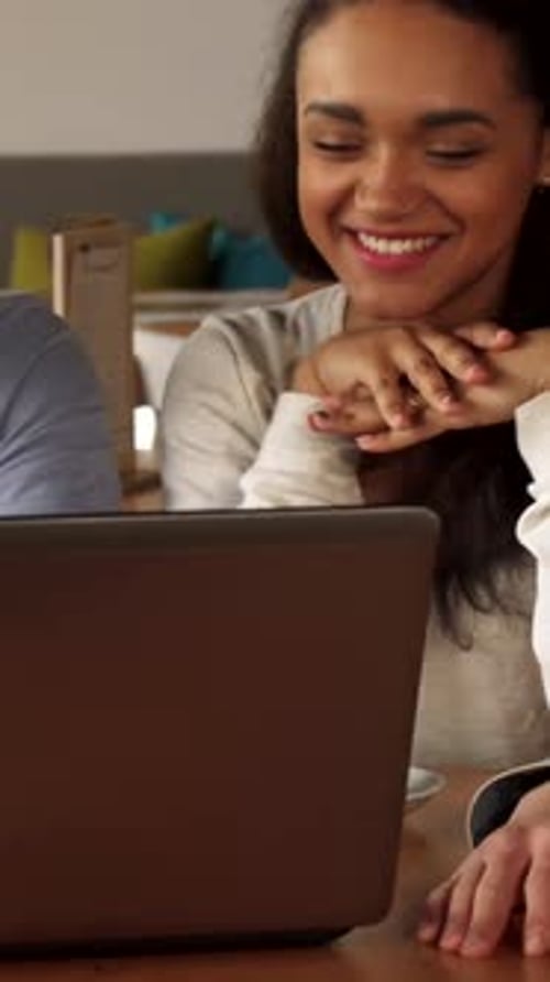 Joyful Friends Sharing Laughter and Ideas Over a Laptop in a Cozy Cafe